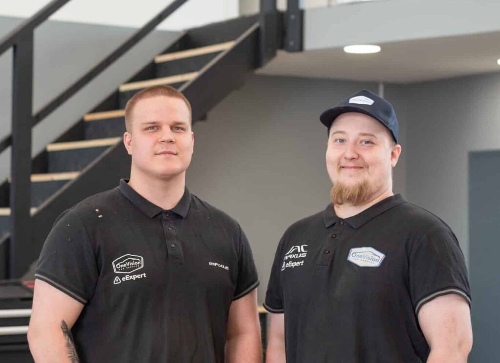 OneVision Car Service autohuolto modernissa autokorjaamossa, taustalla renkaita ja huoltokalustoa.