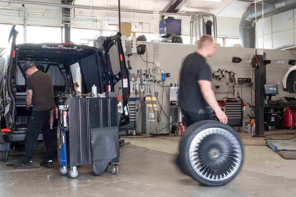 OneVision Car Service autohuolto modernissa autokorjaamossa, taustalla renkaita ja huoltokalustoa.