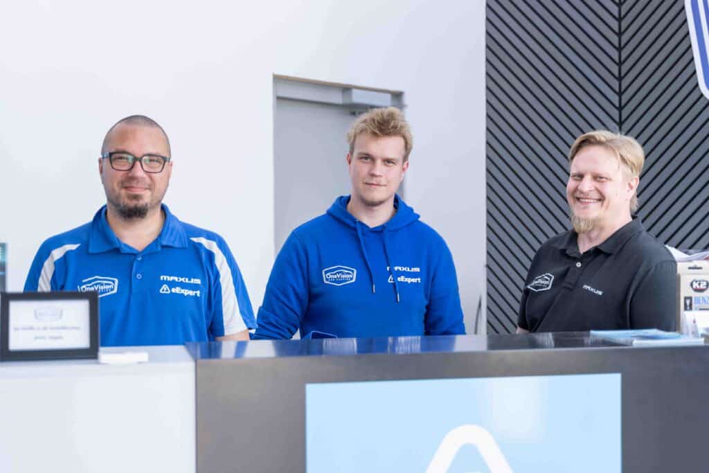 OneVision Car Service autohuolto modernissa autokorjaamossa, taustalla renkaita ja huoltokalustoa.